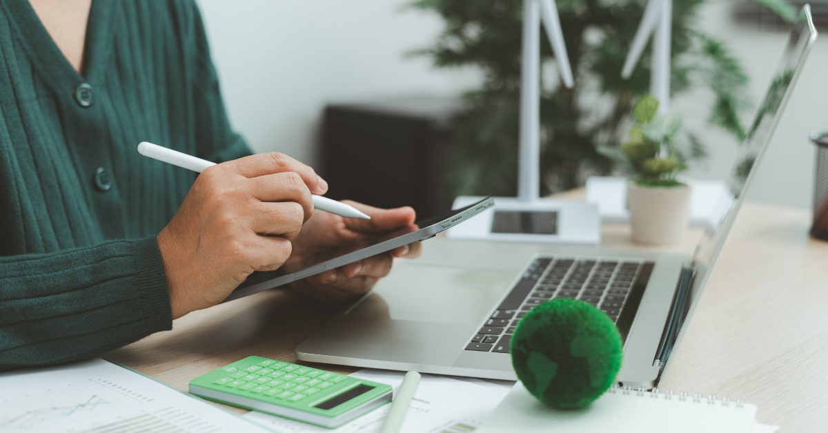Woman sitting at desk with various digital tools like a laptop, iPad and calculator on the table.