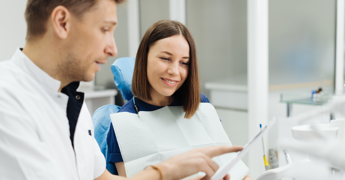 Dentist discussing paperwork with patient in dental chair who is smiling and reading the paper with dentist.